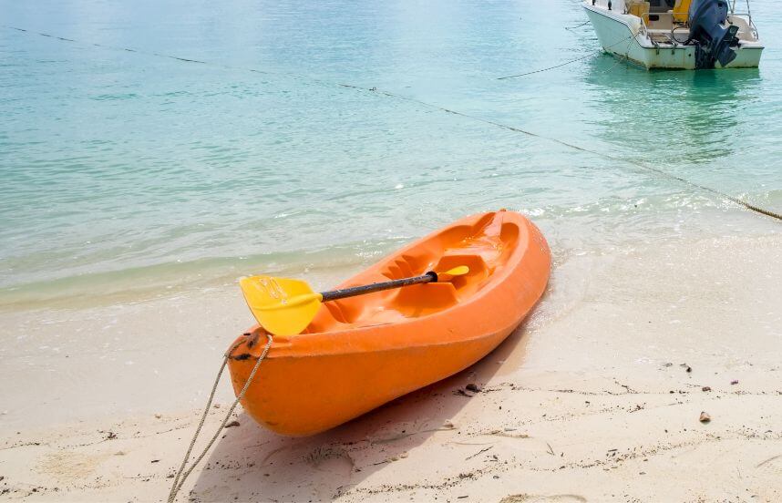 An orange kayak on the sand, held by a kayak anchor