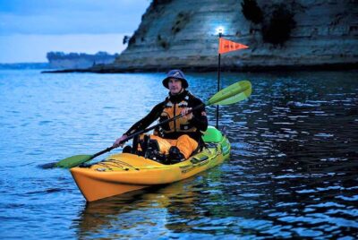 A fully geared kayaker on a yellow kayak with a kayak light.
